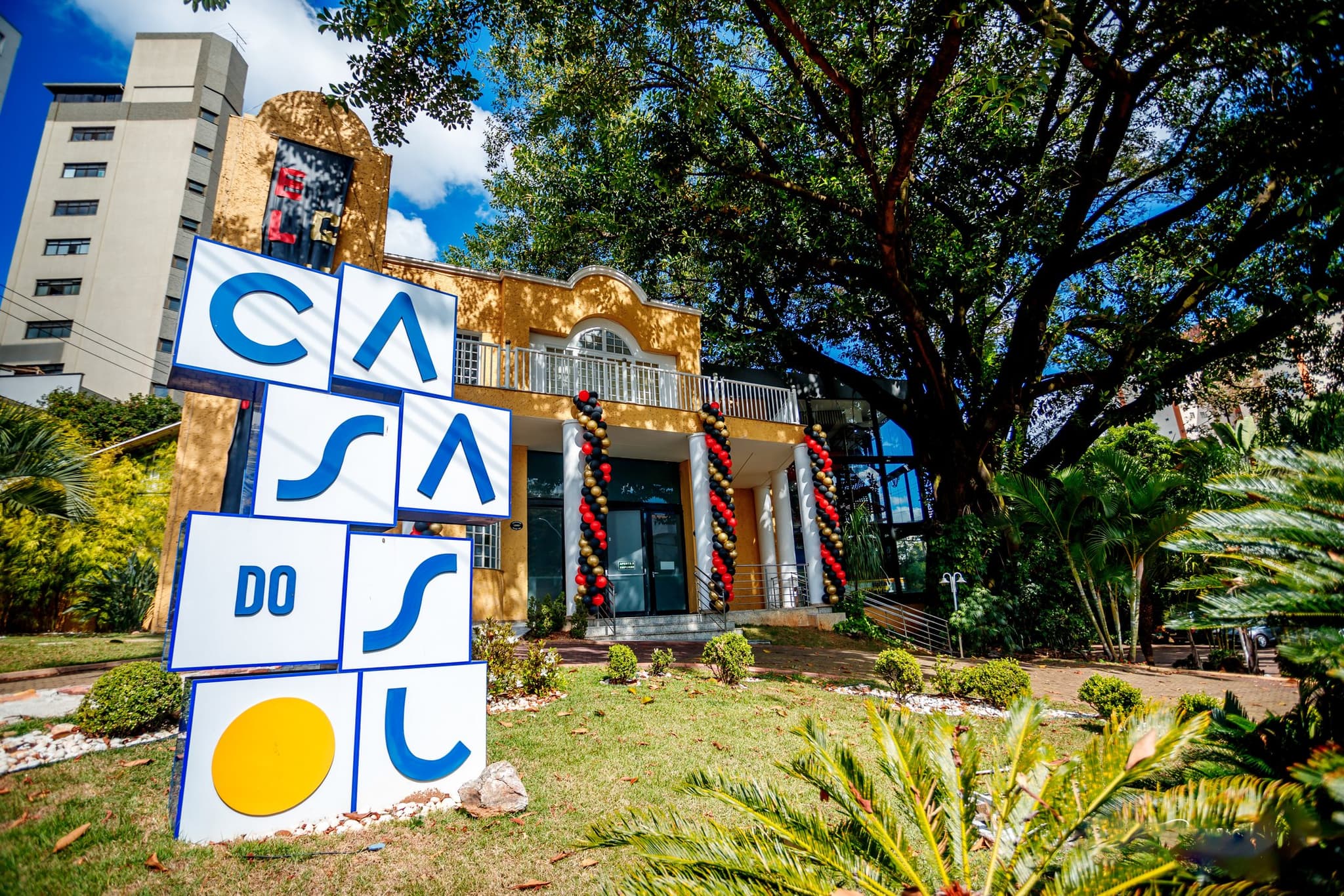 Fachada da Casa do Sol Cidade Nova com letreiro e jardim em luz natural