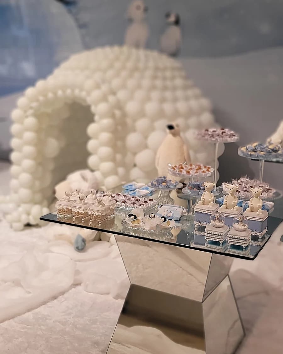 Decoração de inverno com iglu de balões brancos e mesa de doces.