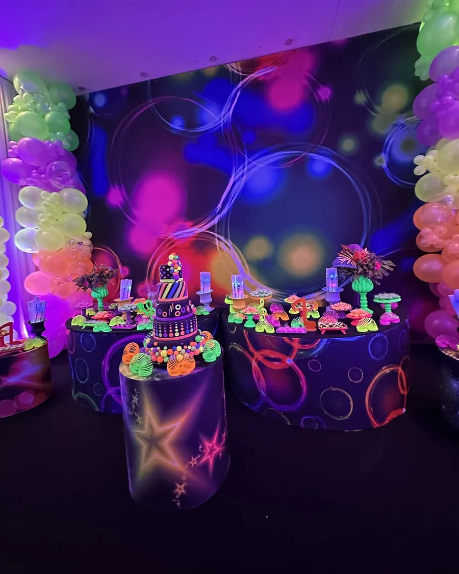 Decoração neon com painel colorido, balões e mesa do bolo.