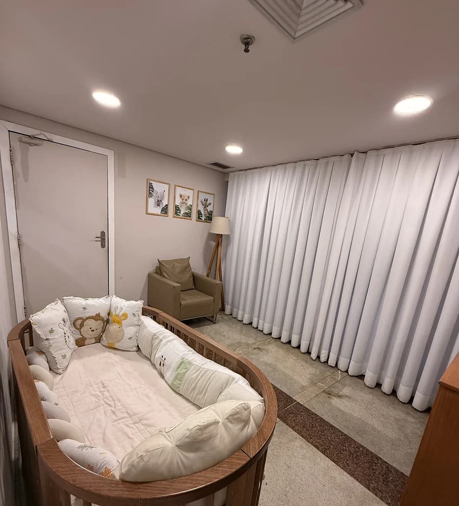 Fraldário com berço, poltrona e cortinas claras.
